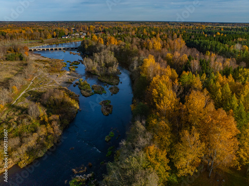 Aerial photo of beautiful autumn landscape. Jagala (Estonian Jägala) river meandering through a dense forest of mixed trees - in gold, orange and green colors. Small bridge crosses the river.  photo