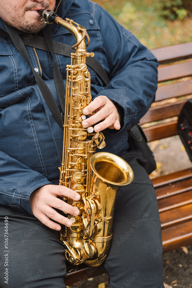 Fototapeta premium A saxophonist performs in a serene park during autumn while seated on a bench surrounded by fallen leaves