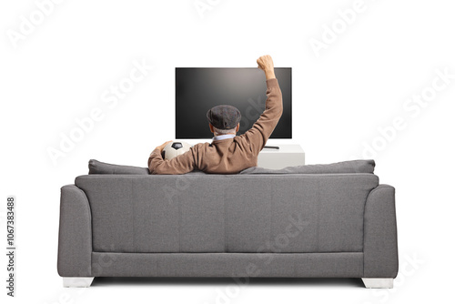 Rear view shot of a senior man on a sofa holding a football and cheering in front of tv photo