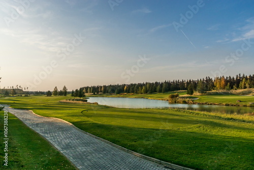 Panoramic view of the green golf course on a clear autumn day. Landscape with ponds on a blue sky background.