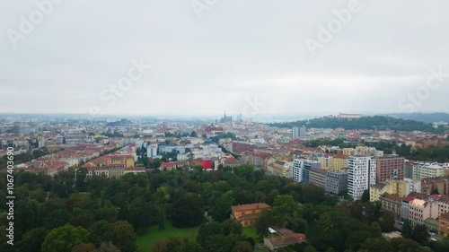 Camera moving right above the city of Brno, Czech Republic. Lush green trees of Park Luzanky fill the foreground, with Spilberk Castle visible in the distance photo