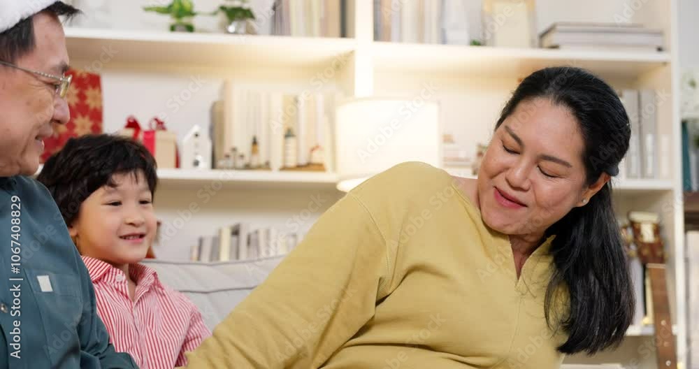Asian family sharing laughter as young grandson hugs grandmother. Grandfather smiles warmly in cozy Christmas setting, capturing love, joy, and festive family connection during holiday season. Asian family sharing laughter as young grandson hugs grandmother. Grandfather smiles warmly in cozy Christmas setting, capturing love, joy, and festive family connection during holiday season.
