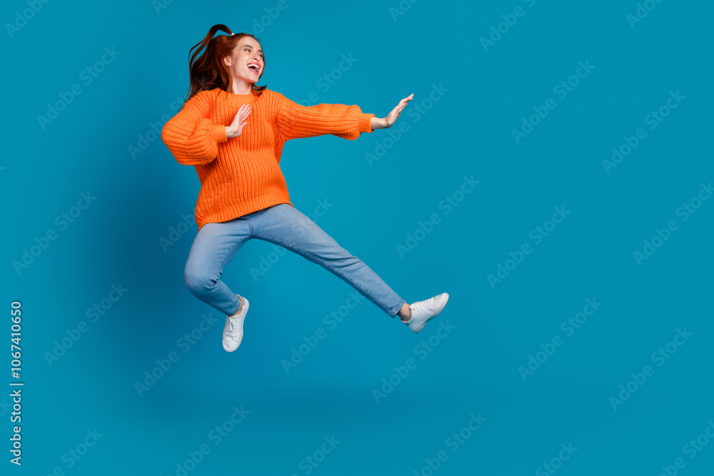 Full length photo of adorable lovely girl orange knitwear sweater jumping high kicking empty space isolated blue color background Full length photo of adorable lovely girl orange knitwear sweater jumping high kicking empty space isolated blue color background