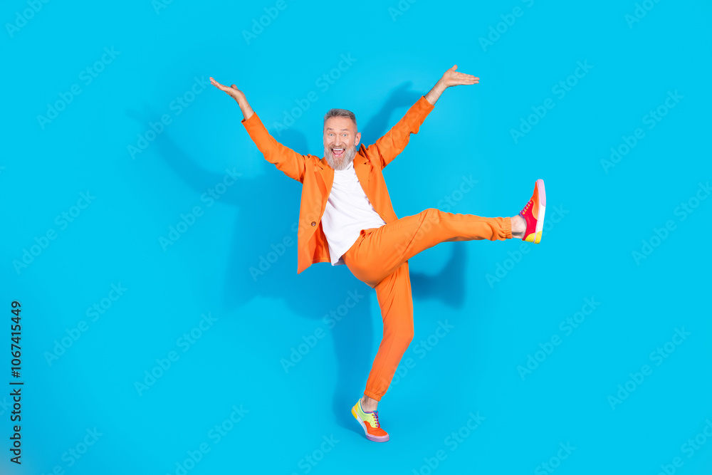 Full length photo of trendy eccentric man dance rejoice wear orange suit isolated on blue color background Full length photo of trendy eccentric man dance rejoice wear orange suit isolated on blue color background