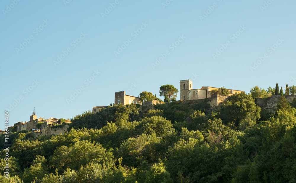 Glimpse of Menerbes in France Provence, with stone houses on the right overlooking the leafy valley below in the warm light of sunset. overall slight sepia tone Glimpse of Menerbes in France Provence, with stone houses on the right overlooking the leafy valley below in the warm light of sunset. overall slight sepia tone