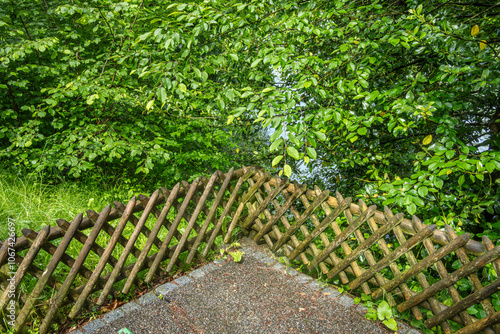 Serene scene of weathered wooden fence, lush green foliage and gravel ground in natures embrace. photo