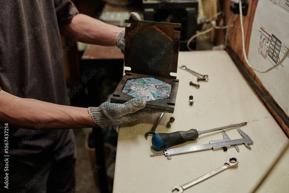 Hands of unrecognizable male technician in protective gloves opening metal press mold with multicolor polymer tile Hands of unrecognizable male technician in protective gloves opening metal press mold with multicolor polymer tile