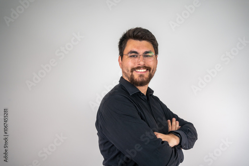 Portrait of happy fashionable handsome man in black shirt and glasses crossing hands and smiling. Photo of a happy young casual man standing. Caucasian handsome man isolated on grey background