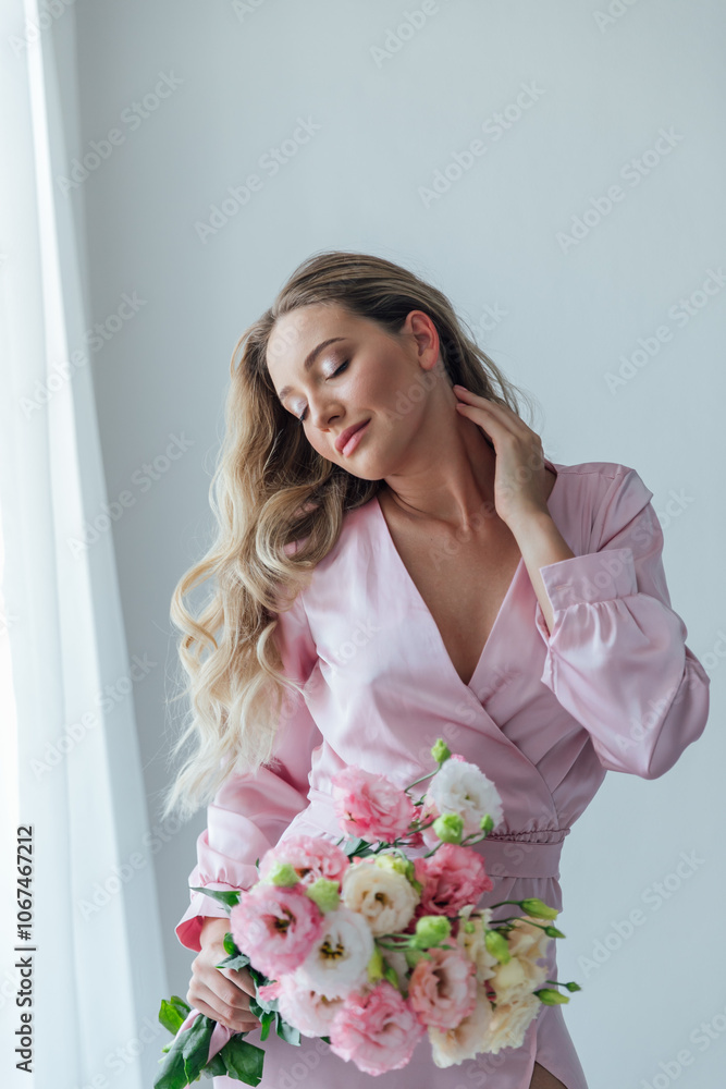 Beautiful fashionable woman in summer pink dress with flowers looking in the mirror