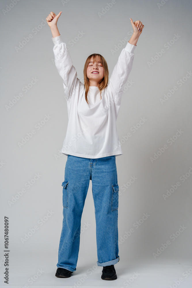 A joyful young girl with long hair wearing a white sweater stands against a plain background A joyful young girl with long hair wearing a white sweater stands against a plain background