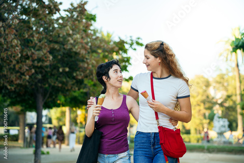 Two young women are walking and eating ice cream in a park