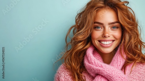 A joyful young woman with long curly hair wearing a bright pink scarf smiles cheerfully, her vibrant expression radiating happiness, against a soft teal background.