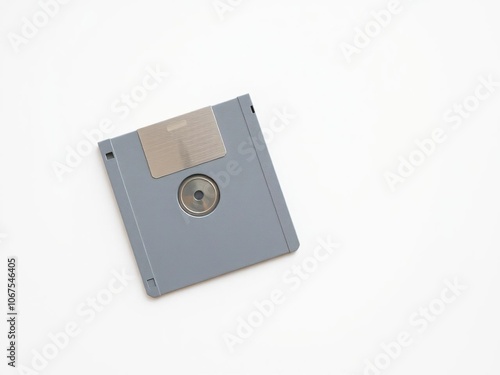 A single floppy disk lies isolated on a minimalist white surface, its color faded to a soft gray from years of exposure, computing history, floppy disk photo