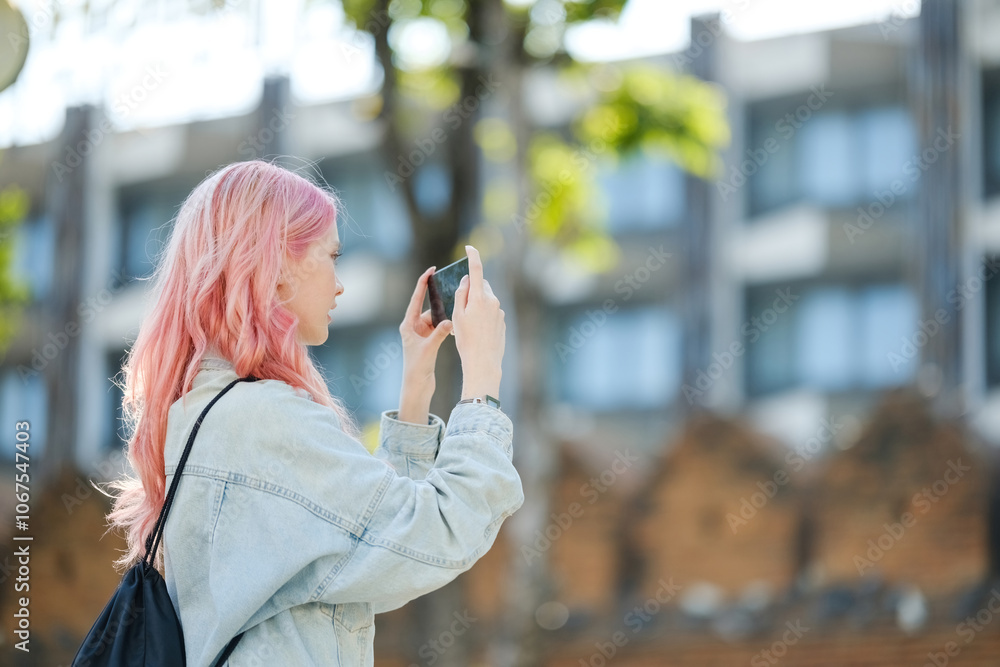 Fototapeta premium A woman with pink hair is taking a picture with her cell phone