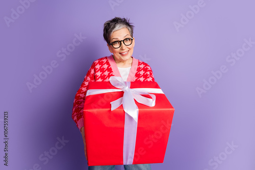 Photo portrait of pretty retired female hold big present box wear trendy red outfit isolated on purple color background