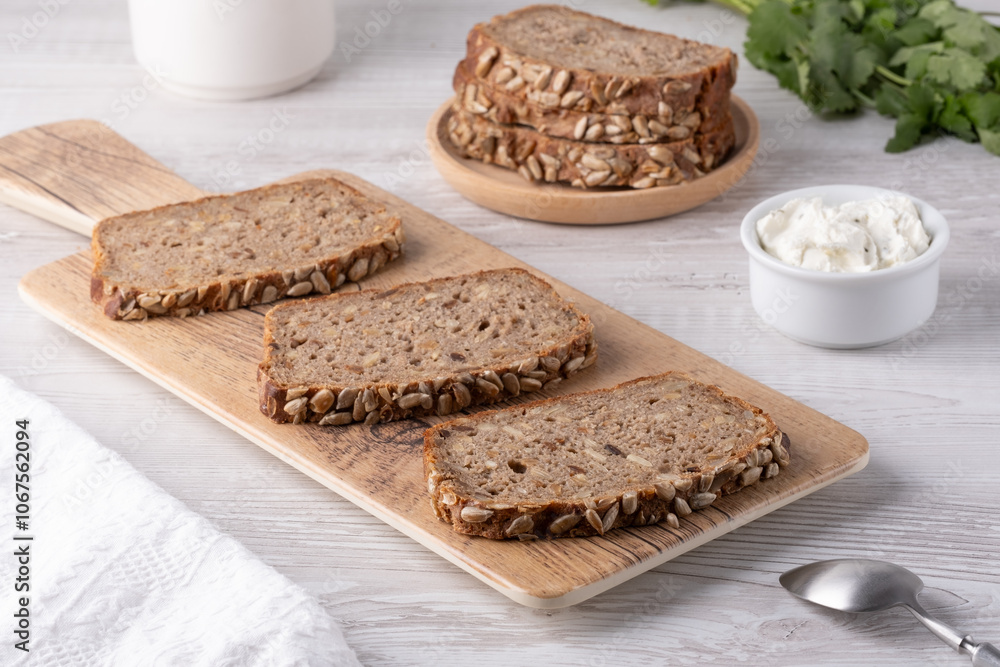 Freshly sliced whole grain bread served on a wooden board with cream cheese and herbs in a bright kitchen setting Freshly sliced whole grain bread served on a wooden board with cream cheese and herbs in a bright kitchen setting