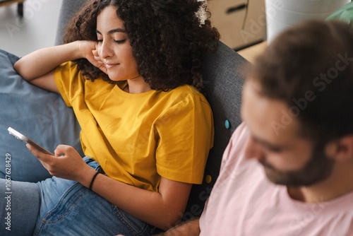 A young woman reclines comfortably on a sofa, holding her smartphone and appearing relaxed in a cozy indoor setting, surrounded by soft furnishings that create a peaceful and laid-back atmosphere. photo