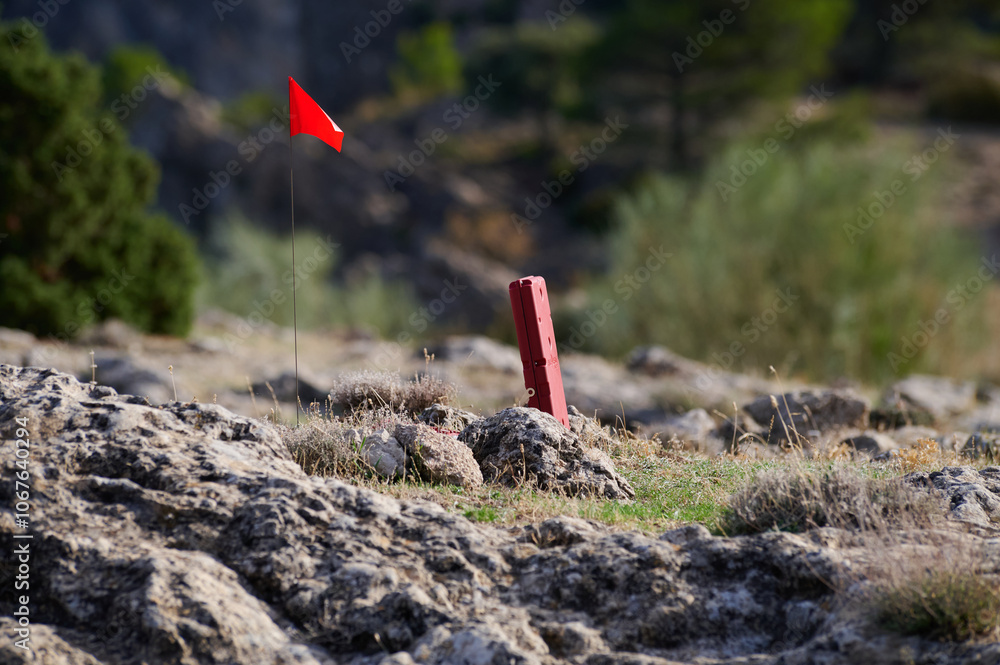 Red flag and marker in rocky outdoor terrain under sunlight Red flag and marker in rocky outdoor terrain under sunlight