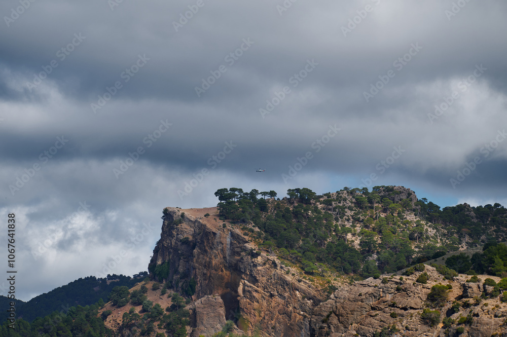 Dramatic cloudy sky over rocky mountain landscape with trees Dramatic cloudy sky over rocky mountain landscape with trees