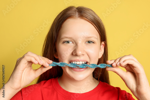 Teenage girl eating tasty gummy candy on yellow background