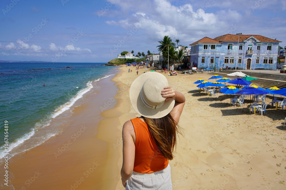 Obraz premium Summer holiday in Brazil. Back view of young woman in Praia do Bonfim beach looking the Forte do Monte Serrat fort in Salvador de Bahia, Brazil.