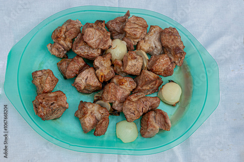 pieces of grilled pork meat with onions on a blue plate top view