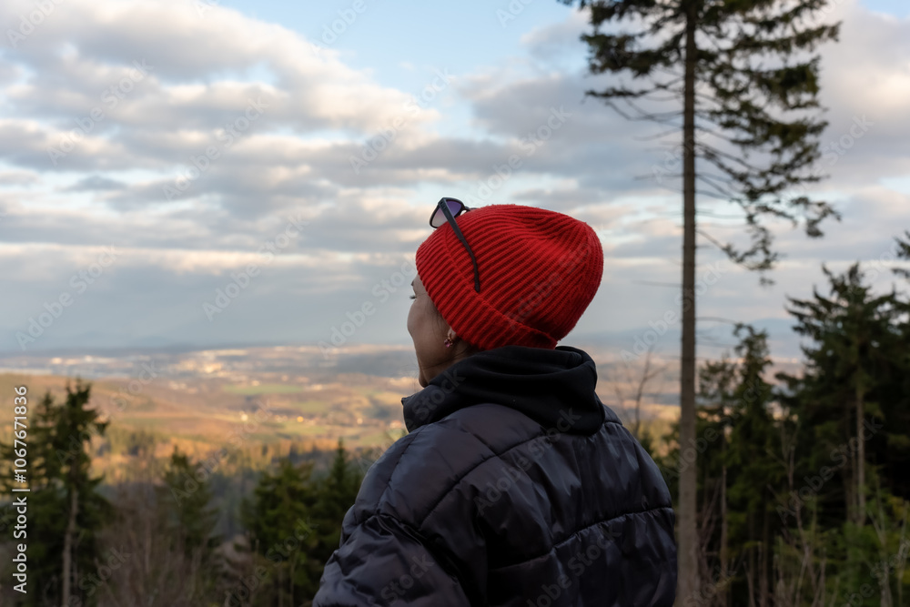 Woman in red knitted hat enjoying serene forest landscape at sunset. Concept of inner peace, outdoor adventure and union with nature Woman in red knitted hat enjoying serene forest landscape at sunset. Concept of inner peace, outdoor adventure and union with nature