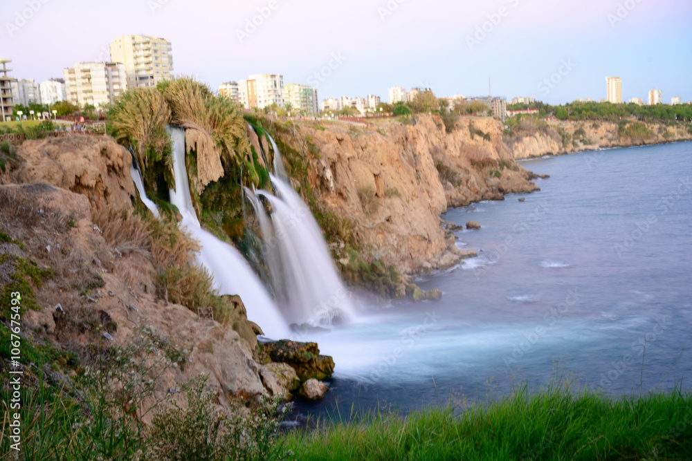 Scenic view of Duden Waterfall in Antalya, Turkey, cascading from cliffs into the Mediterranean Sea with a faint rainbow visible.
Scenic view of Duden Waterfall in Antalya, Turkey, cascading from cliffs into the Mediterranean Sea with a faint rainbow visible.