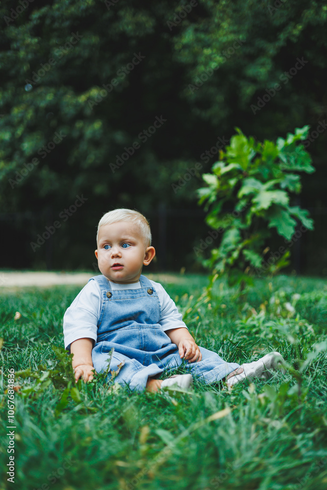 A one-year-old blond boy in a t-shirt and denim dungarees walks in the fresh air. Self-development of the child. A one-year-old blond boy in a t-shirt and denim dungarees walks in the fresh air. Self-development of the child.