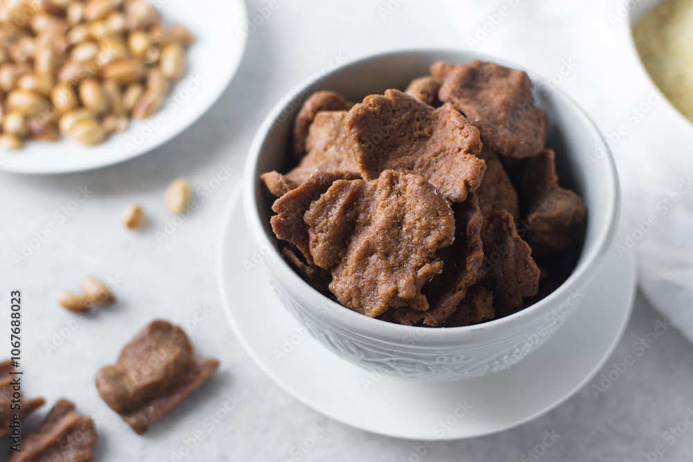 Overhead view of kuli-kuli and roasted peanuts on a white plate, top view of nigerian groundnut cakes and groundnuts on a plate Overhead view of kuli-kuli and roasted peanuts on a white plate, top view of nigerian groundnut cakes and groundnuts on a plate