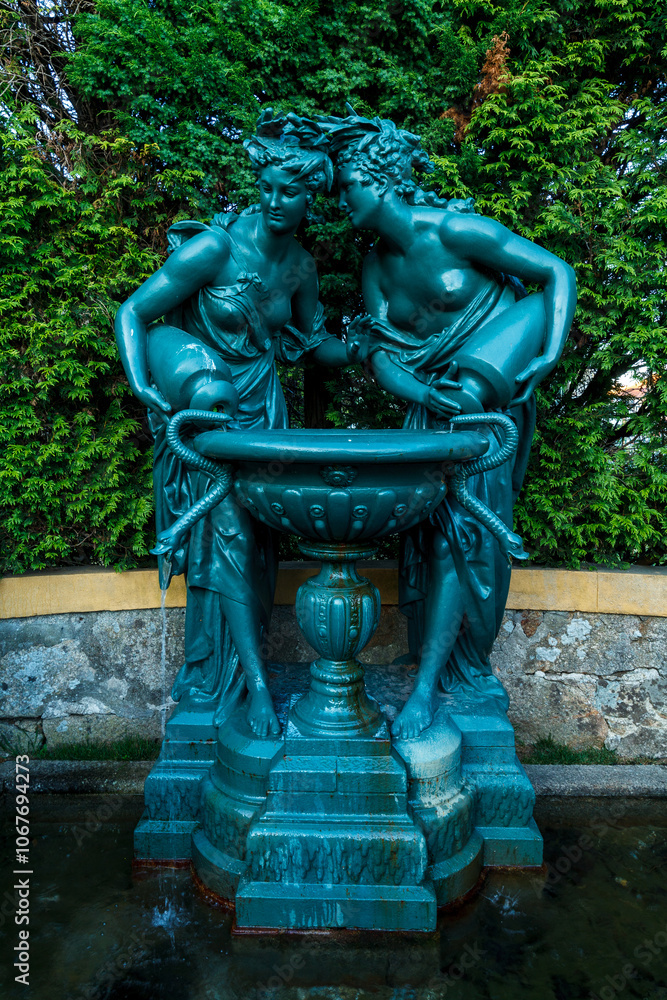 green statue of two classical female figures in an intimate pose, each leaning towards a basin they hold together green statue of two classical female figures in an intimate pose, each leaning towards a basin they hold together