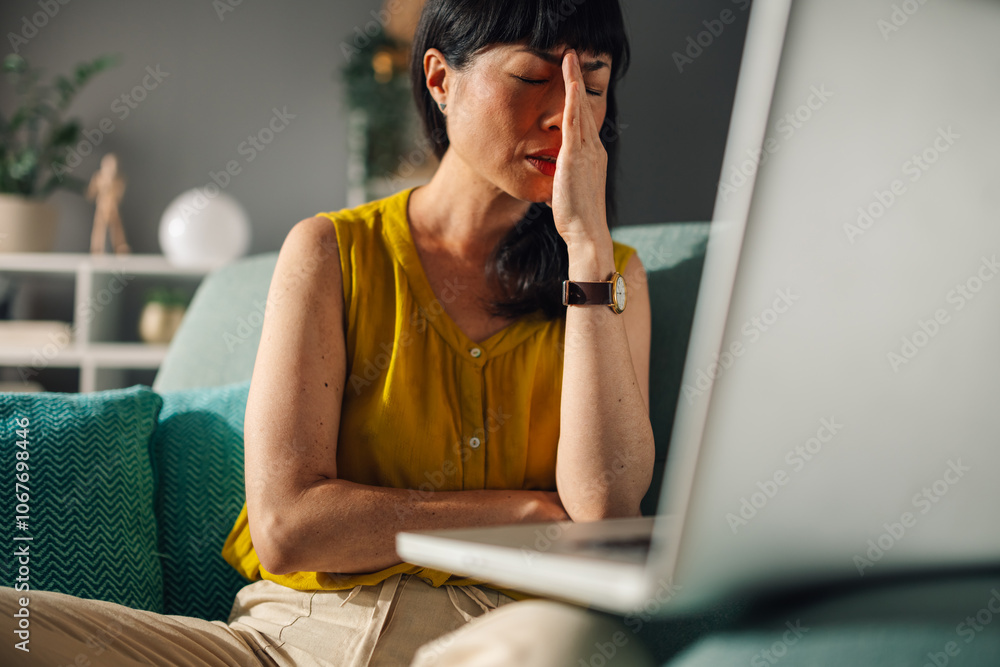 Asian woman in yellow top on green couch working on a laptop at home. Asian woman in yellow top on green couch working on a laptop at home.