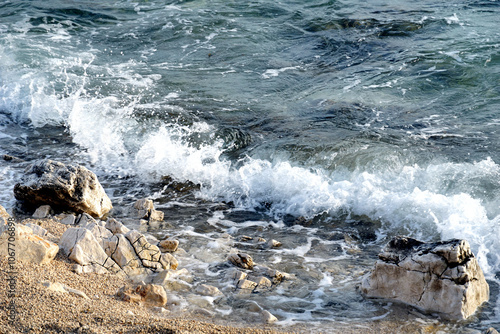 Clear sea water with big splashing and foamy wave that hitting the pebble beach