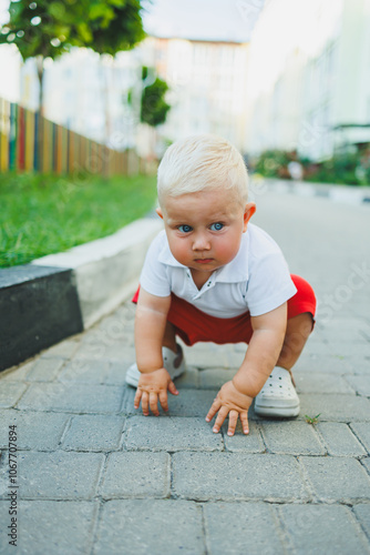 A toddler boy in a white t-shirt and shorts on a walk in the summer. The child runs and plays in the fresh air.