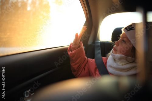 a child sitting in a car, gazing thoughtfully out the window. The soft light illuminates the child's face, highlighting a sense of wonder and curiosity as they observe the world passing by. 