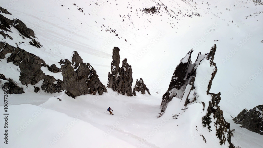 Snowy mountain slopes tower with rugged cliffs, where a skier navigates through pristine, challenging terrain.