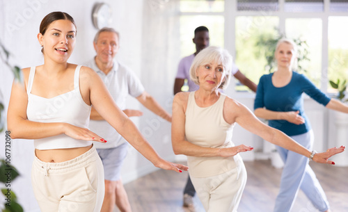 Smiling attractive young girl visiting group choreography class with adult people of different ages, learning modern dynamic dances. Concept of active lifestyle.. photo