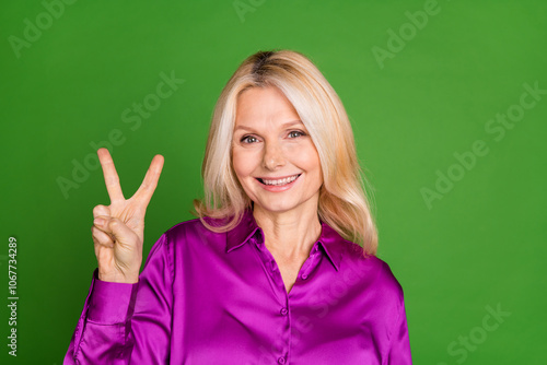 Photo portrait of lovely pensioner lady show v-sign dressed stylish purple satin garment isolated on green color background