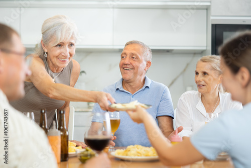 Group of joyful seniors at family dinner drinking and chatting at table in kitchen