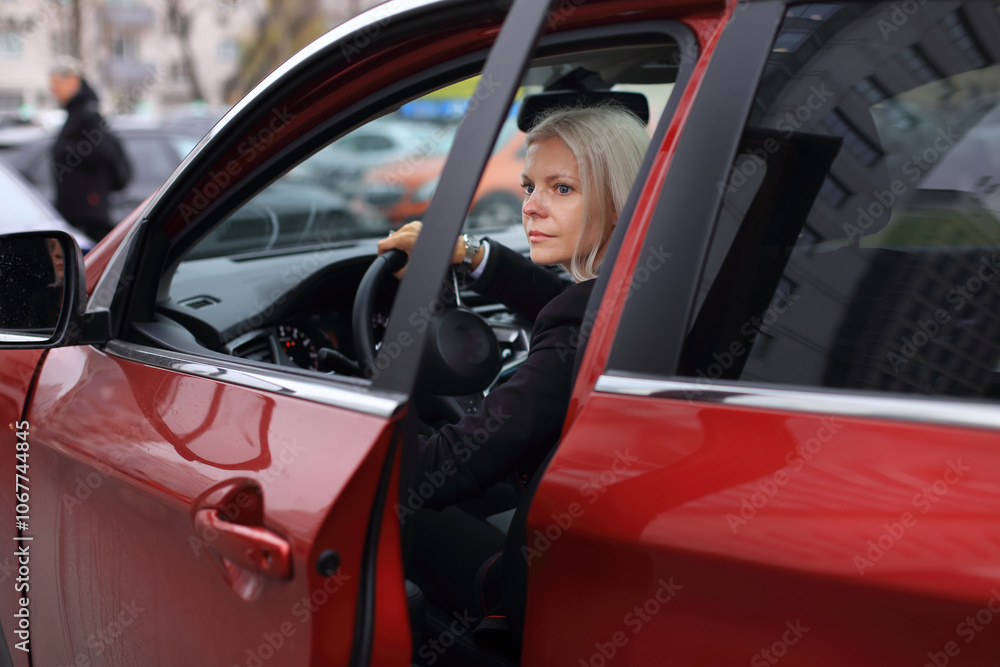 A professional businesswoman sits confidently in her stylish red car, parked outside a modern business center. A professional businesswoman sits confidently in her stylish red car, parked outside a modern business center.