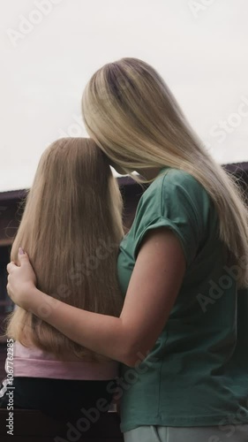 Loving mother hugs little daughter sitting on terrace of eco hotel looking at old distant mountains with mist cloud backside view slow motion