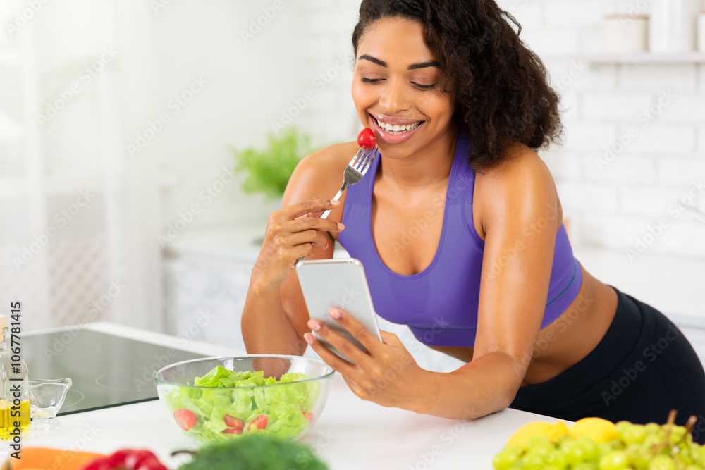 Healthy Eating Concept. Beautiful black woman eating salad using application, sending message on smartphone device