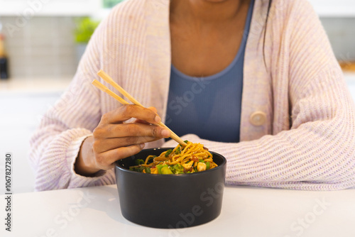 Asian woman enjoying delicious noodles with chopsticks at home, savoring every bite photo