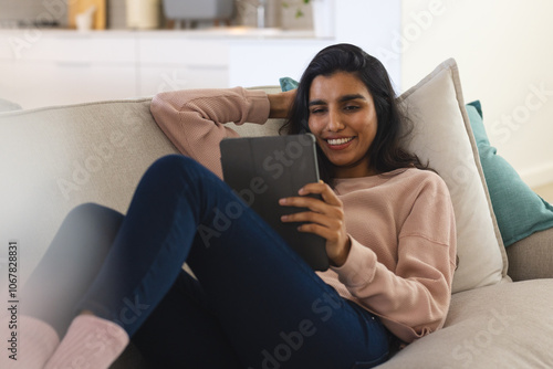 Relaxing on couch, Asian woman smiling while using tablet at home photo