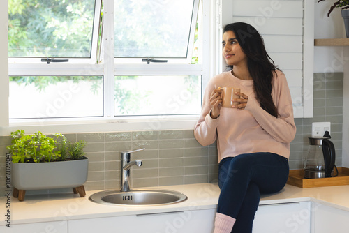 Relaxing in kitchen, Asian woman enjoying coffee by window, feeling peaceful, at home photo