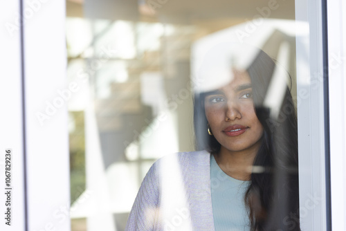 Asian woman gazing thoughtfully through window, reflecting on holiday season, at home photo