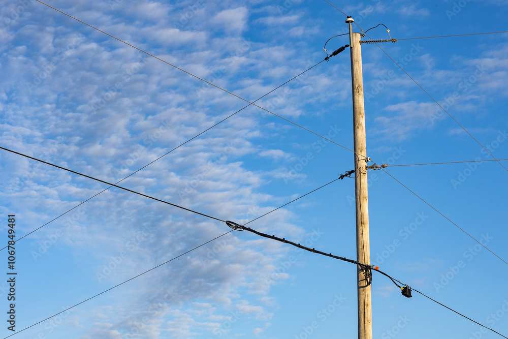 An electric pole with cross wires against a blue sky with altocumulus clouds. 