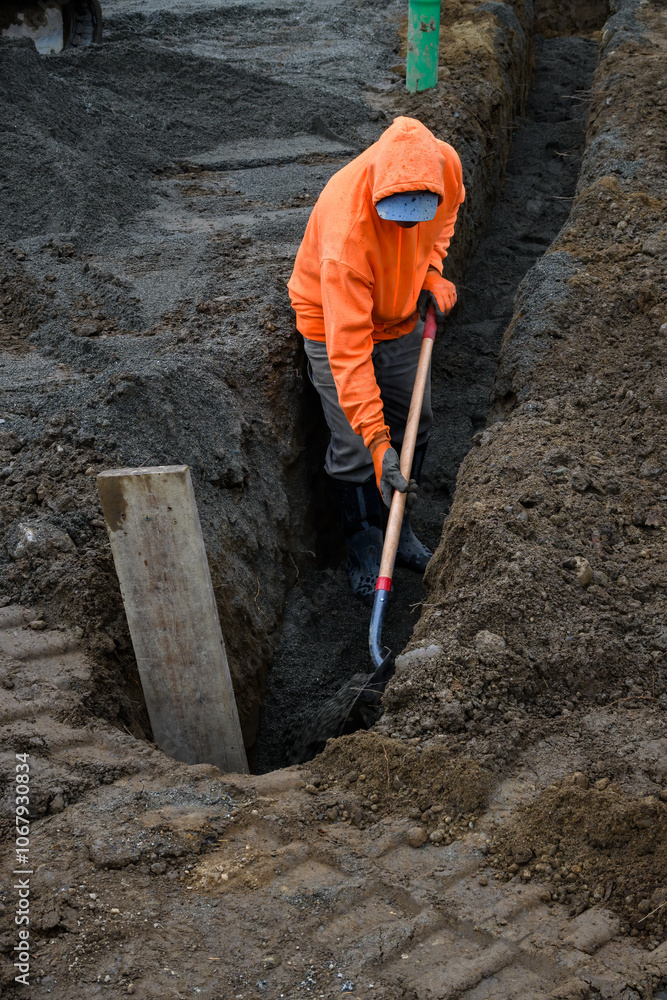Construction worker in a trench dug out to install underground PVC pipe conduits, wearing an orange safety sweatshirt and working with a shovel
Construction worker in a trench dug out to install underground PVC pipe conduits, wearing an orange safety sweatshirt and working with a shovel