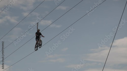 Extreme cyclist wearing a helmet is riding a bicycle on a high wire suspended in the air, performing a daring stunt against a cloudy sky