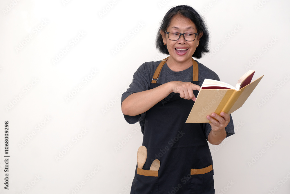 Asian housewife wearing apron, reading a book of recipes to prepare breakfast Asian housewife wearing apron, reading a book of recipes to prepare breakfast